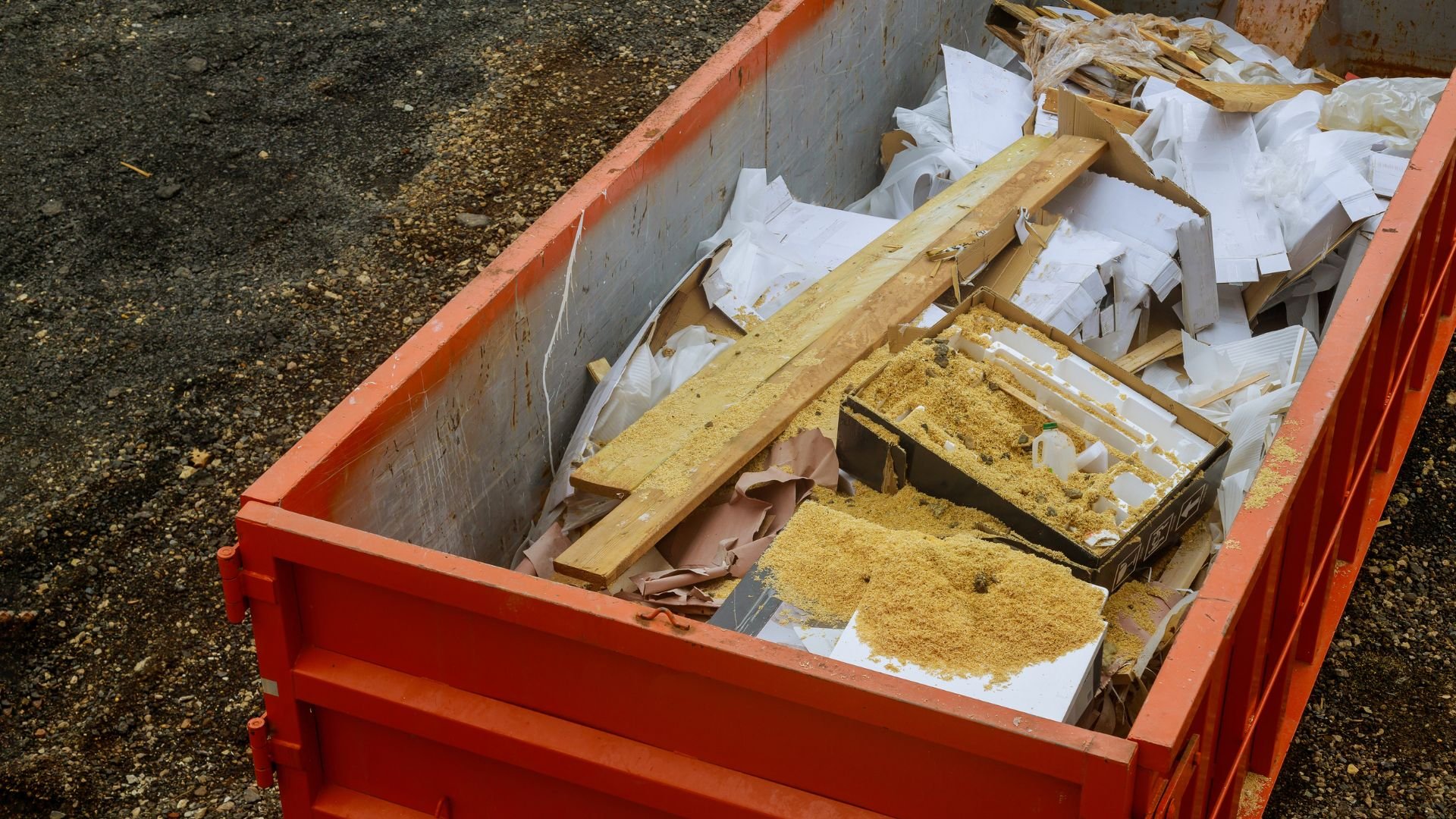 Red dumpster filled with construction debris, wood, and sawdust